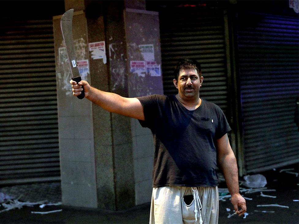 A shop owner holds a machete after staying up all night to protect his business during widespread looting and protests in Durban, South Africa, on 12 July 2021