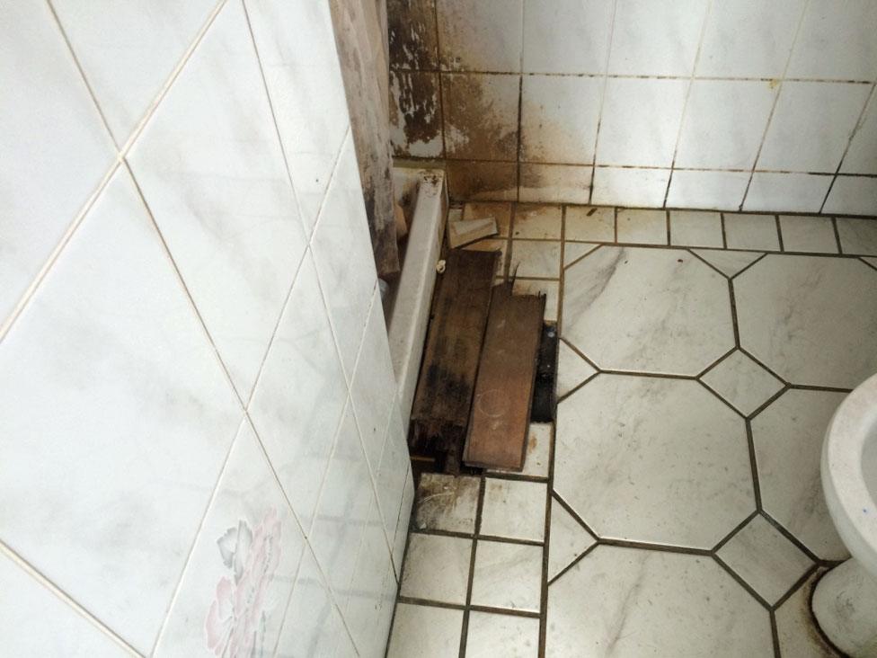 A bathroom, dirty and patched up with broken wooden boards