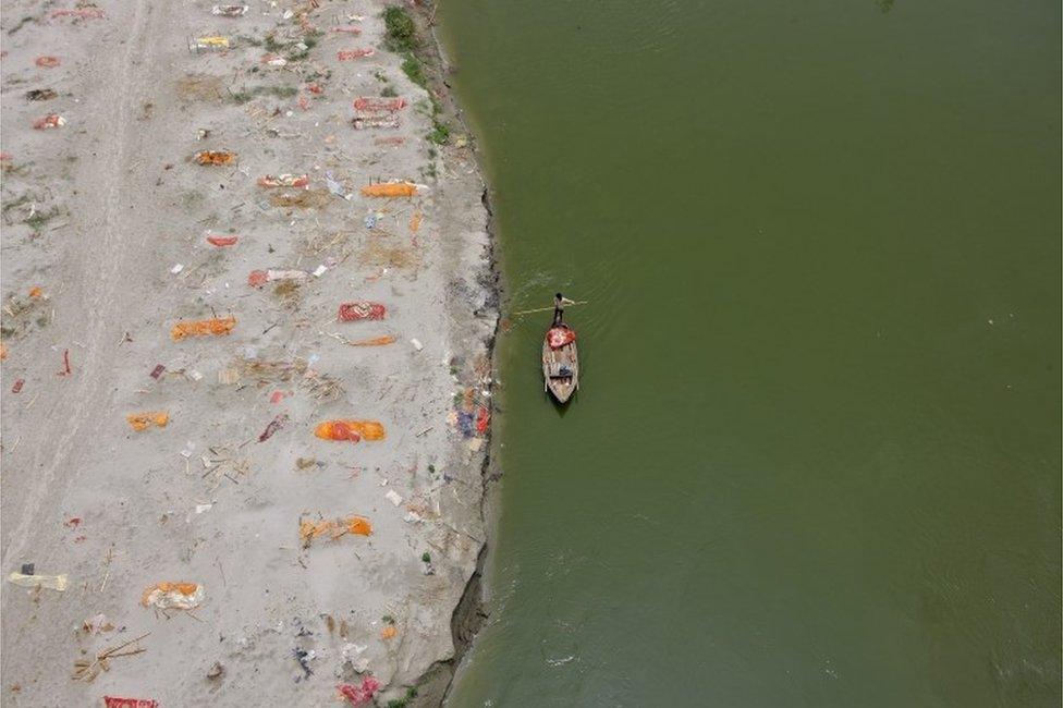 A man rows his boat past shallow sand graves of people, some of which are suspected to have died from the coronavirus disease (COVID-19), on the banks of the river Ganges in Phaphamau on the outskirts of Prayagraj, India, May 21, 2021