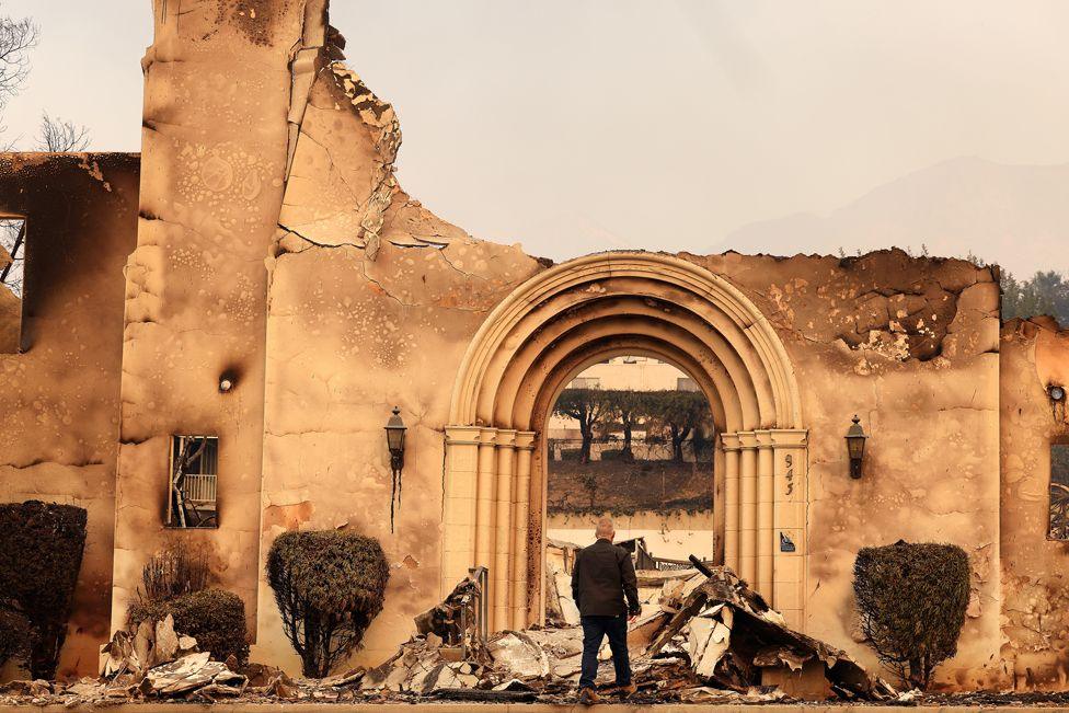 A man stands and looks at the remains of the Altadena Community Church, burned down by the Eaton fire