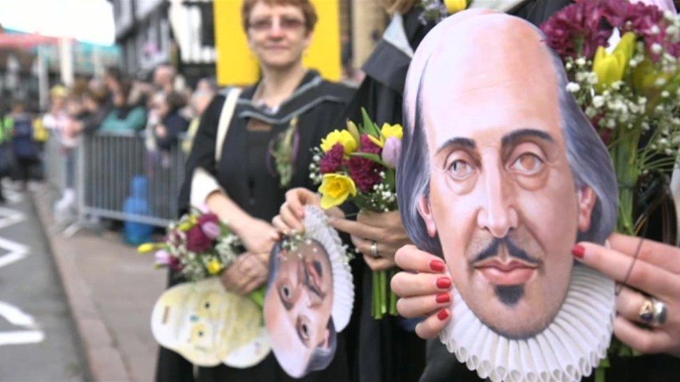 A shakespeare mask being held at the Stratford carnival