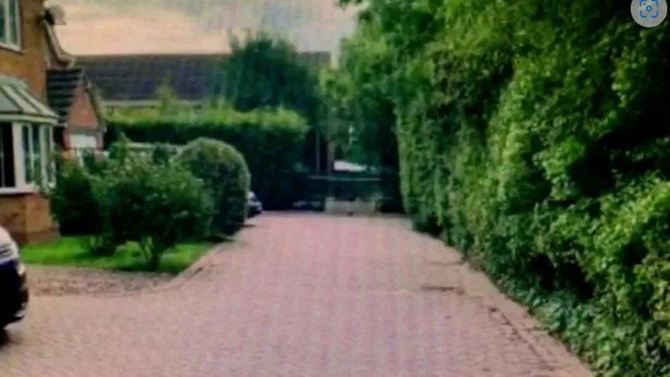 Block pave driveway with large hedge on one side and house on the other