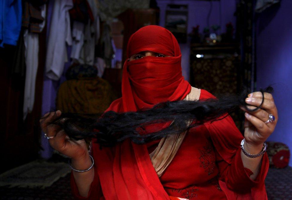 A veiled Kashmiri Muslim woman displays her braid, which was cut off while she was unconscious