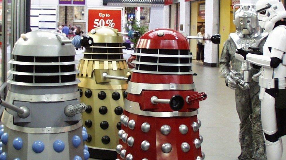 Three daleks in a shopping centre - one in grey, another gold and the other red