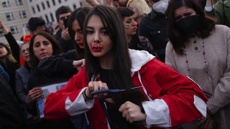 A young protester with red ink on her face that spells "HELP" cuts her hair with scissors during a demonstration against the death of Mahsa Amini on September 23, 2022 in Berlin, Germany