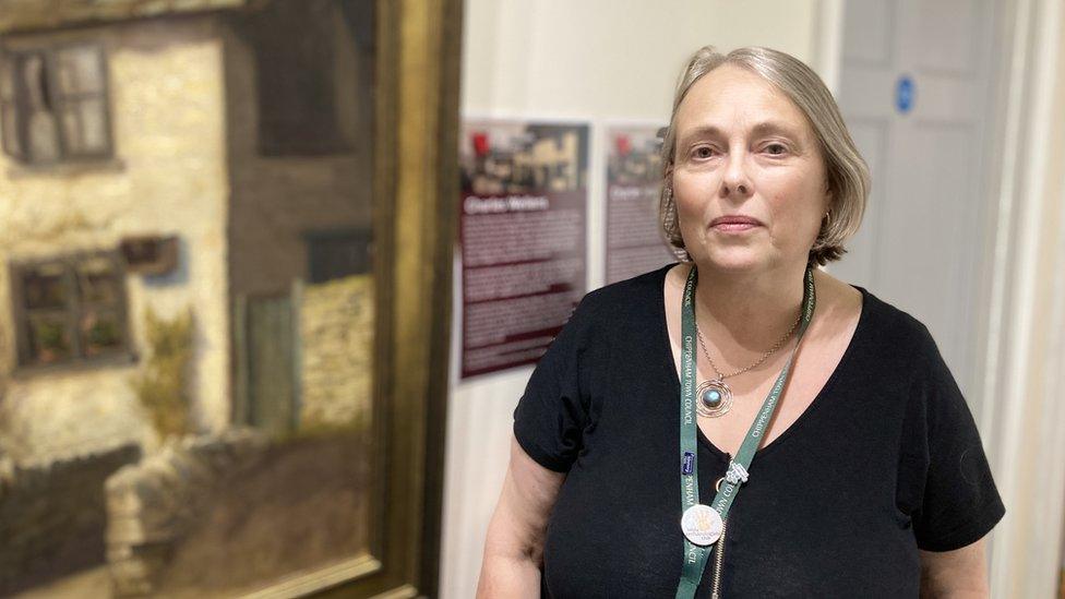 Elaine Davis in a black top in front of a painting looking into the camera