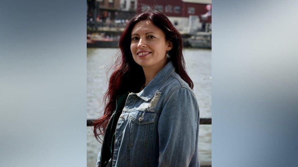 Noemi Antonelli wearing a denim jacket, standing in front of a body of water