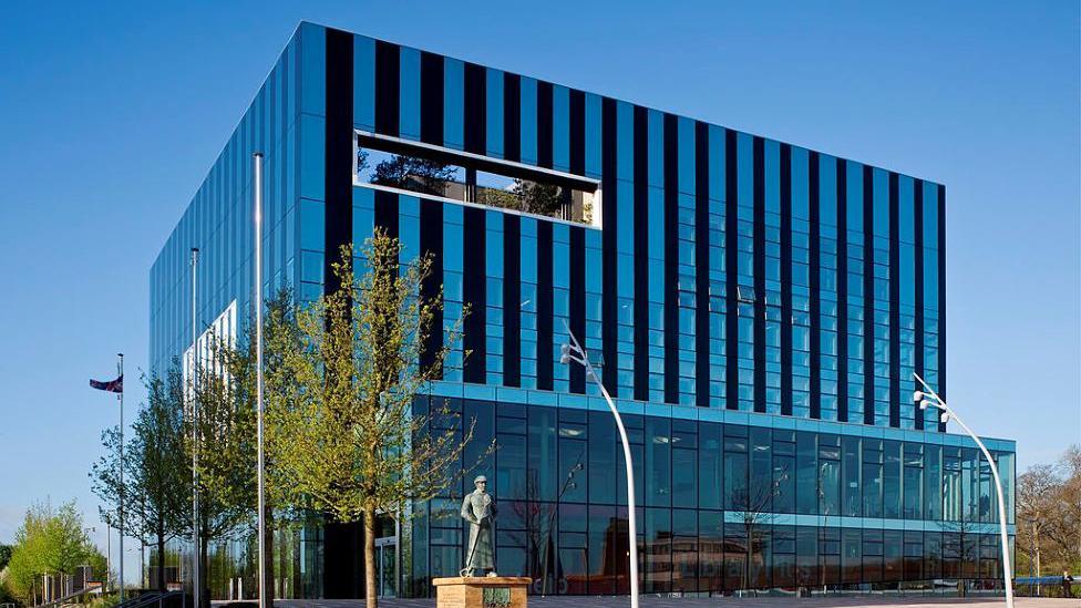 A glass building in a cube design in the middle of a town square.