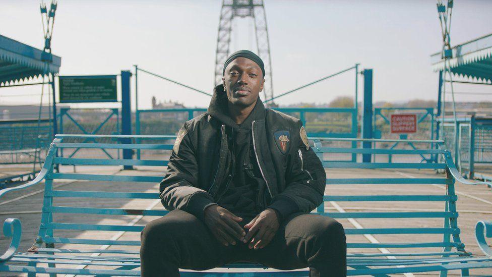 Rapper Lemfreck sits on a blue bench on Newport Transporter Bridge 