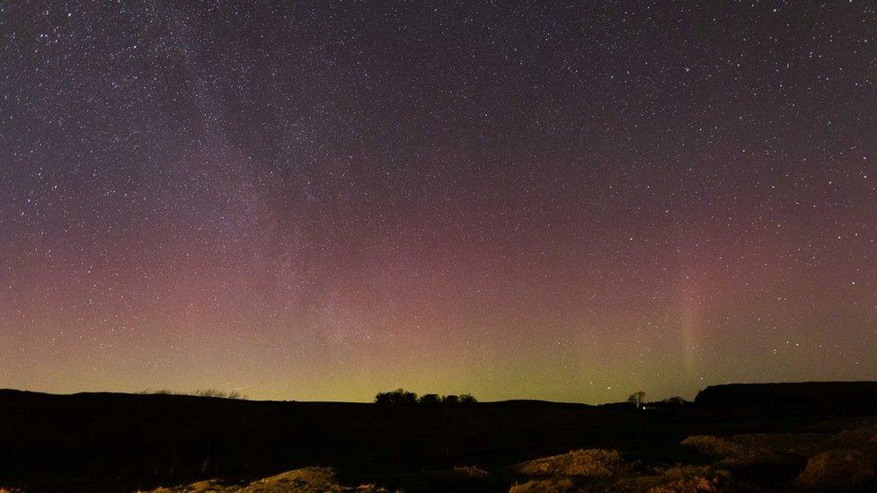 Night sky with lots of stars and a yellow, green and pink hue from the Northern Lights