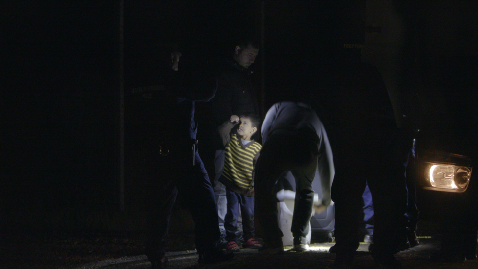 A child in a striped top is surrounded on all sides by uniformed police that he is only waist-high to in this night-time photograph