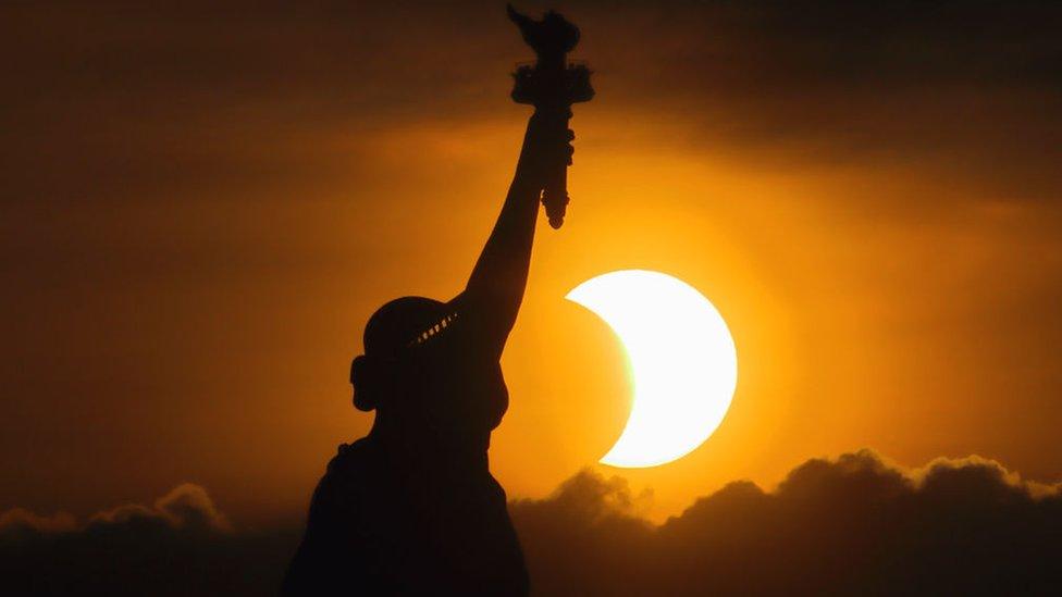 Partially eclipsed Sun next to the Statue of Liberty.