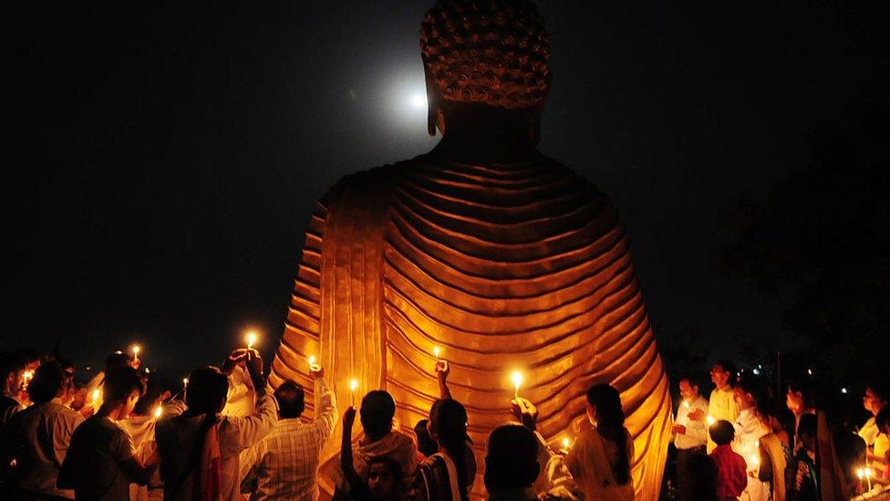 People lighting candles by a Buddha statue at full moon.