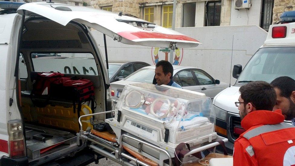 Members of the Lebanese Red Cross wheeling a baby in an incubator on a stretcher from the hospital into the back of an ambulance