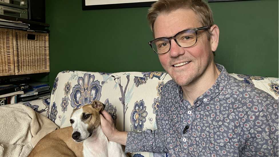 A man sitting on a sofa with a brown and white dog