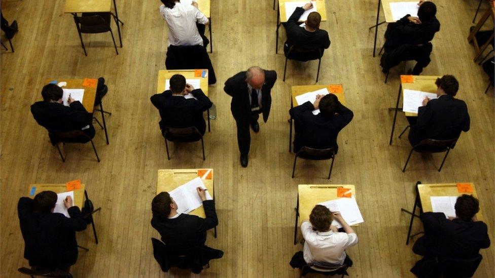 School students taking an exam as an invigilator walks among them, stock image