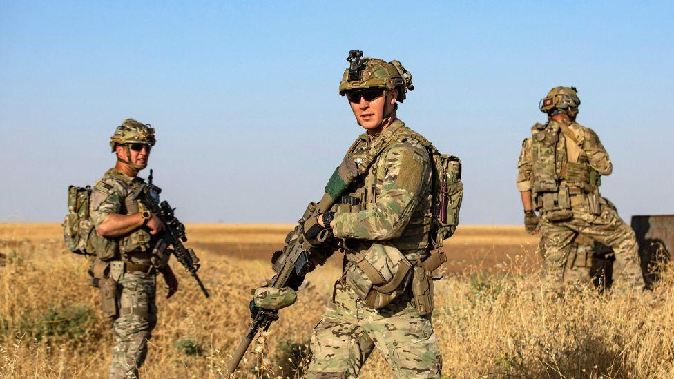 A group of three US soldiers wearing camouflage and carrying rifles on patrol in a field