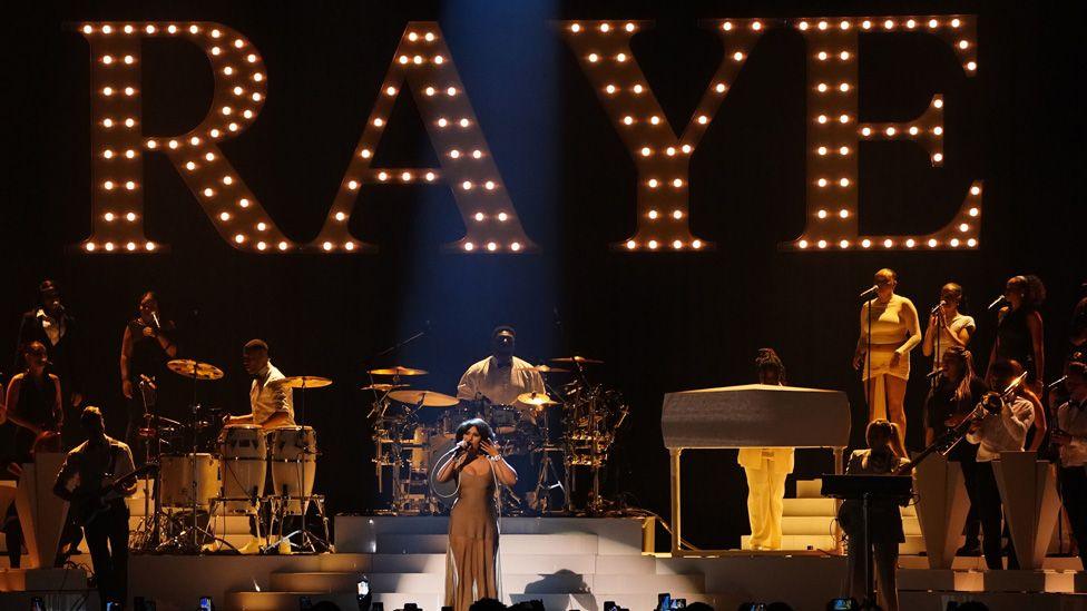 Raye on stage in front of her name in giant lights