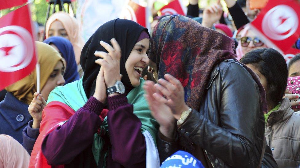 Tuisian girls smile at each other while clapping at a rally to celebrate the fifth anniversary of the Arab Spring