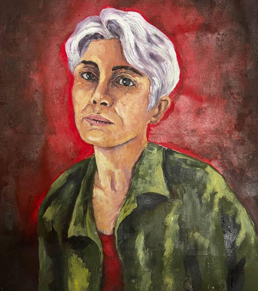 A painting of Pakhshan Azizi shows her with short grey hair, wearing a green shirt with a red top underneath it. She looks thoughtful. The background is deep red.  