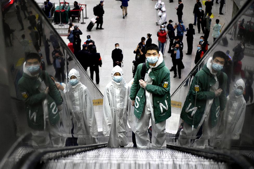 Travellers wearing protective gear ride an escalator