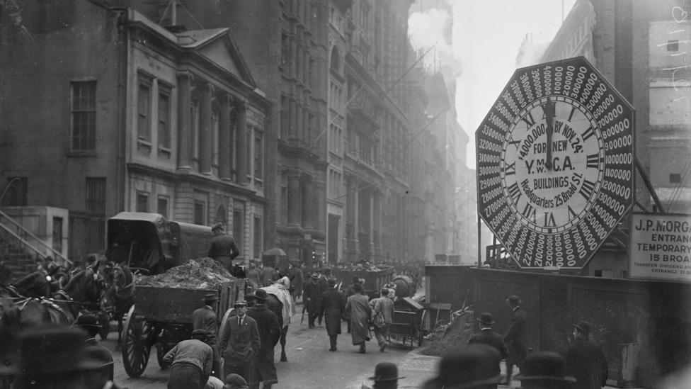 Wagons trundle along Manhattan Streets past a YMCA clock sign