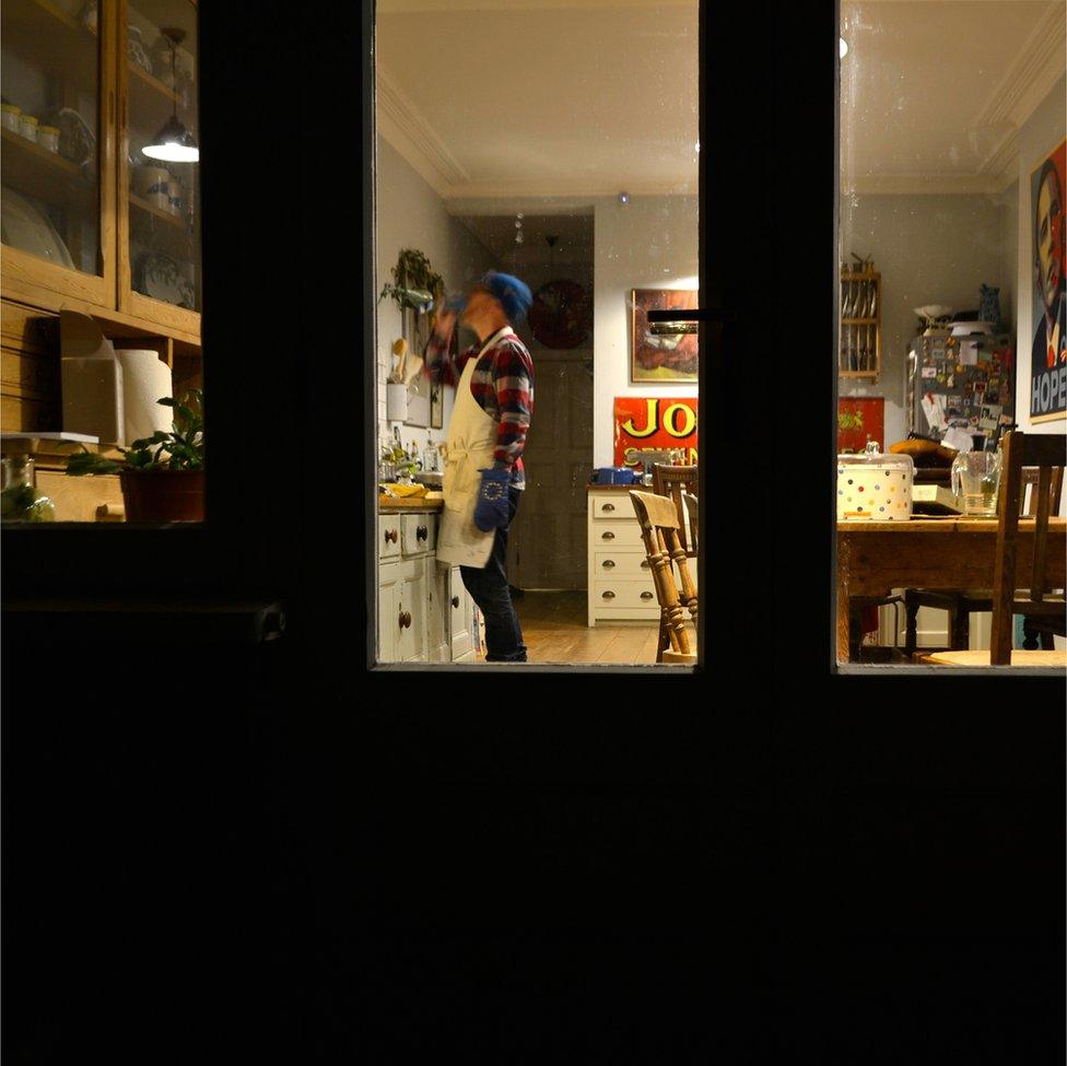 An image of a man drinking in his home whilst wearing oven mittens with the EU symbol on