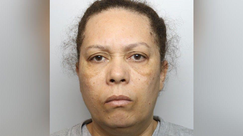 Veronique John in a picture taken by police. She is wearing a grey top and is looking straight at the camera. Her hair is tied back.