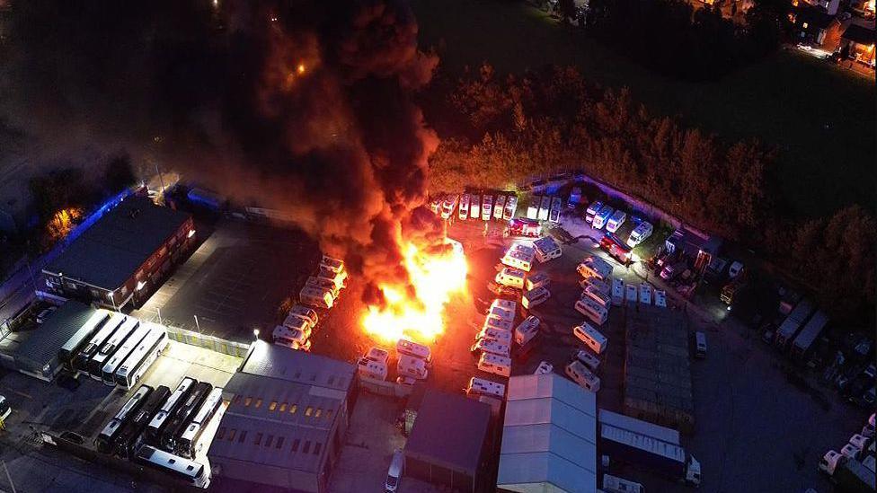 Drone image of a fire at the yard in Chadderton showing the flames and plumes of smoke. There is a big fire in the middle of parked caravans.