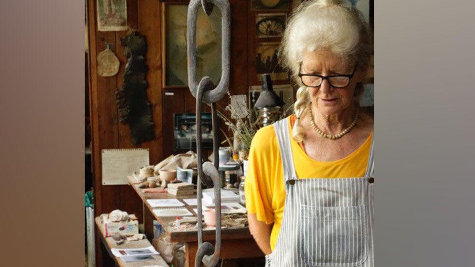 Elspeth Owen looking down in her studio, with a table and bench behind piled with ceremics