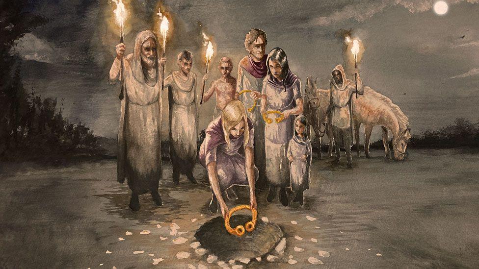 An artist's impression by Craig Williams of a group of men and women and a child dressed in lose clothing, some holding torches, one man standing towards the back, holding a torch and in front of two horses. A woman is bending down in front of the group to place a gold Iron Age torc into a pit in the ground. It is night so the image is in grey tones, with the moon to the far right and shadowy trees glimpsed on the left.