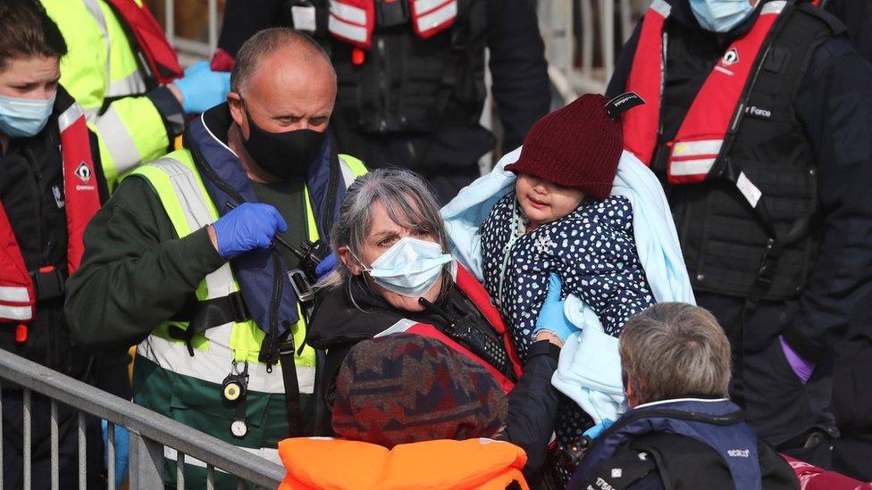 A young girl amongst a group of people thought to be migrants is carried by a Border Force officer as they are brought in to Dover