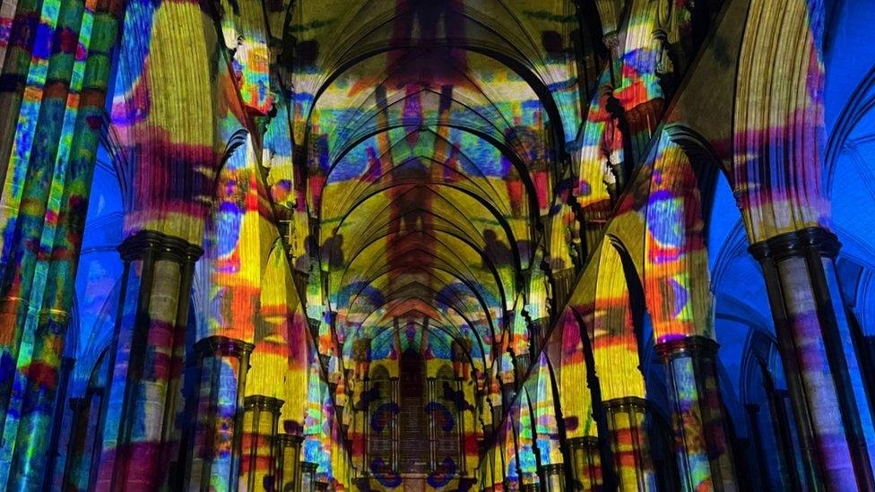 Image of the Sarum Lights exhibition at Salisbury Cathedral. Colourful lights are projected onto the interior of the building.