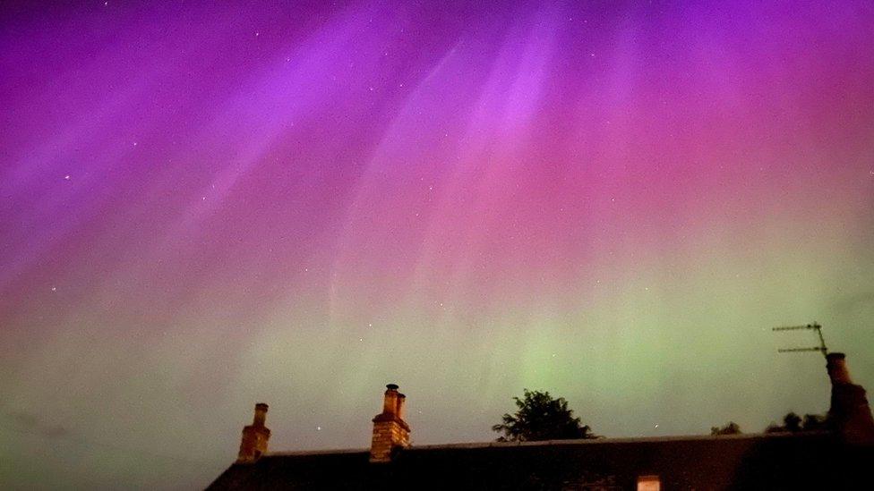 Above a house, the sky is green, pink and purple