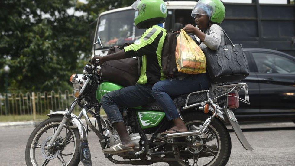 A Nigerian motorbike rider drive through traffic gridlock in Lagos with his passenger