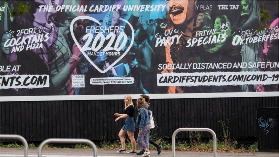 Young women walking next to university poster