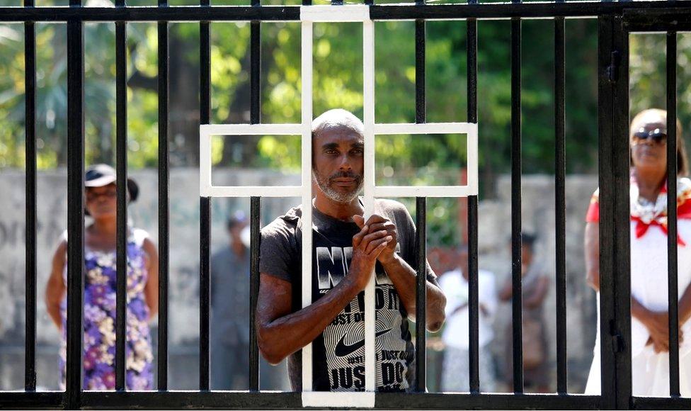 People stand at the gate of a church closed to the public during a mass held on Easter Sunday, amid the outbreak of the coronavirus disease (Covid-19), in Port-au-Prince, Haiti, 12 April 2020