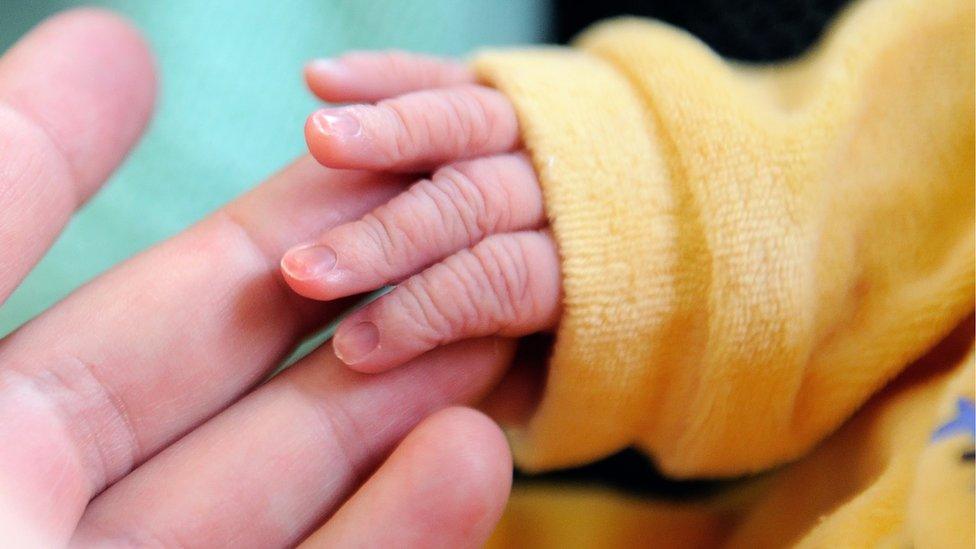 A close up of a newborn baby holding its mother's hand