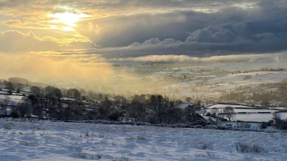 The sun breaks through the clouds above the fields in a snow covered valley in North Yorkshire