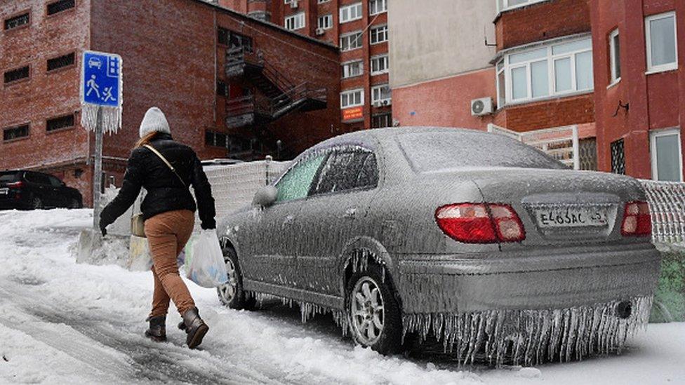 A woman walks past a car covered with ice after a recent freezing rain in eastern Russia