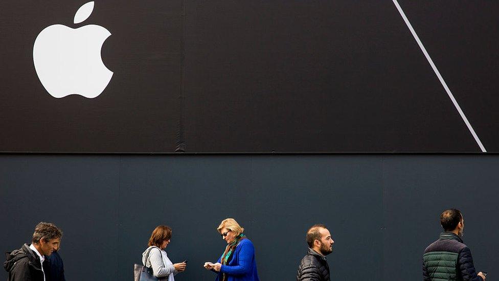 Pedestrians walks past Apple logo