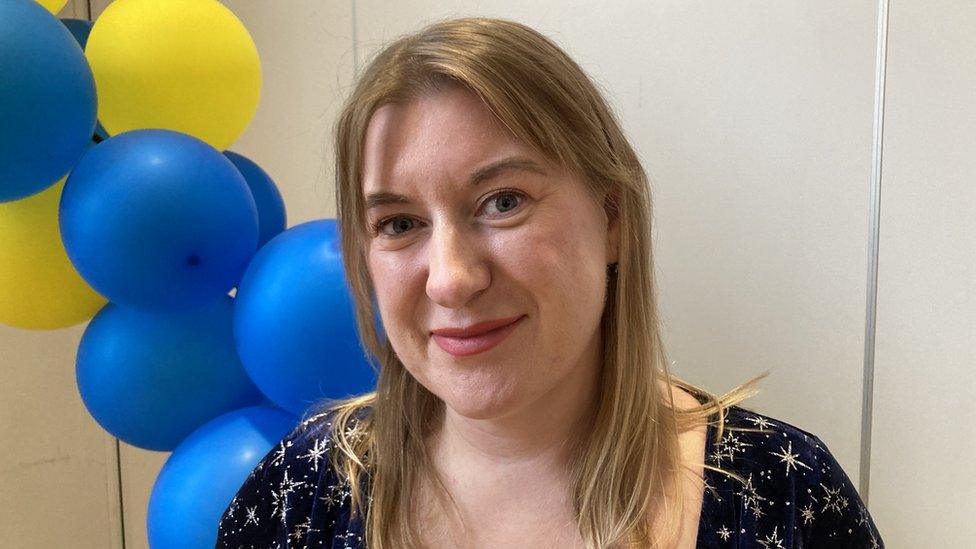 Woman with long light brown hair stands in front of balloons.