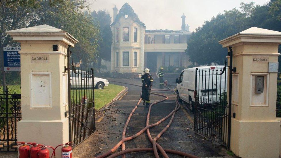 Firefighters check a burnt house, used as a University of Cape Town students' residence, as a forest fire burns out of control on the foothills of Table Mountain