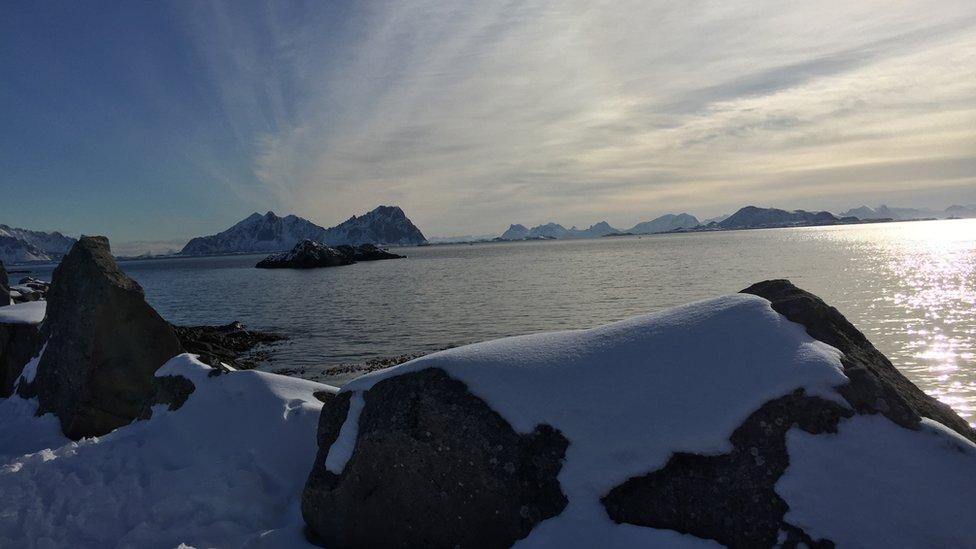 An open expanse of Norwegian water is seen over the tops of some snow-covered rocks