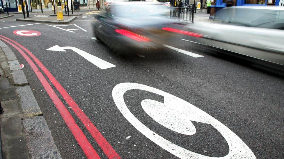 Cars drive pass congestion charge signs