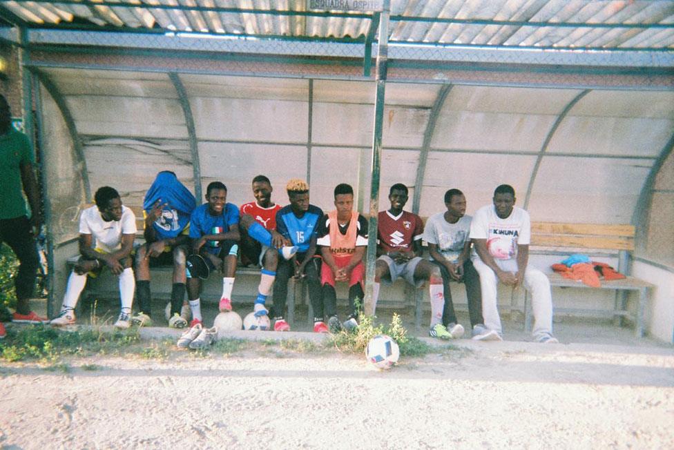 A group of football players watch by the side of the pitch