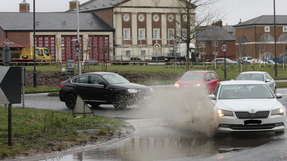 Cars driving through floodwater on a roundabout on the A35 at Poundbury