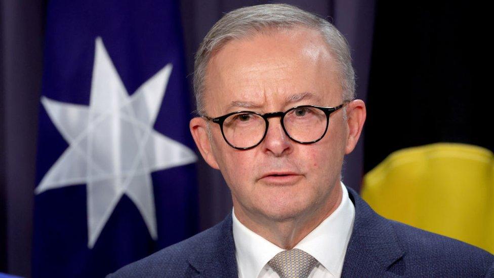 Anthony Albanese stands in front of an Australian flag