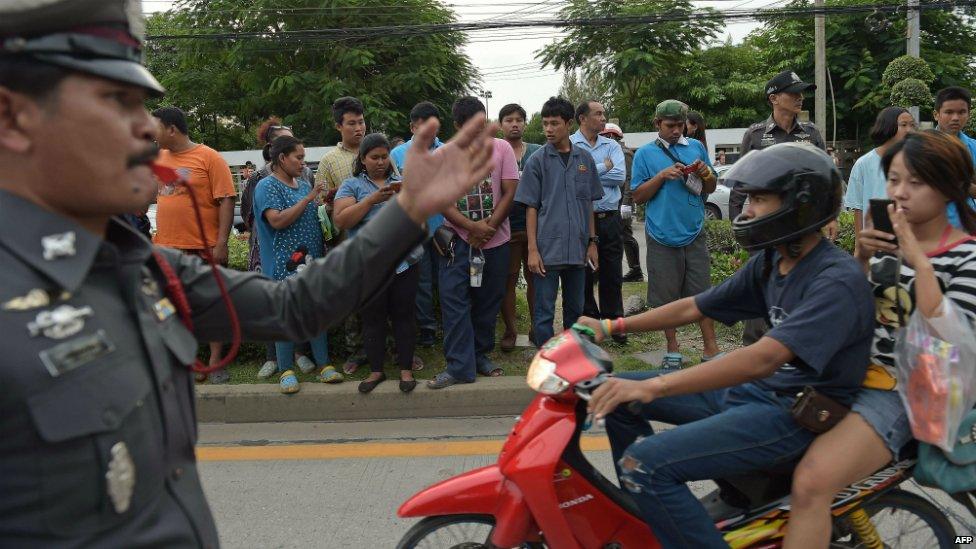 Onlookers pass a policeman outside the apartment where police detained a suspect in the Bangkok shrine bombing - 29 August 2015