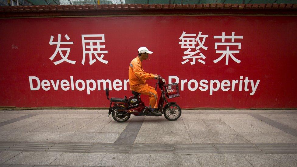 A maintenance worker rides a scooter past banners reading "Development" and "Prosperity" in English and Chinese on a street in central Beijing